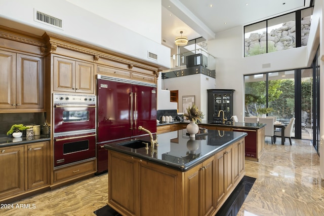 kitchen with sink, built in fridge, an island with sink, decorative backsplash, and double wall oven