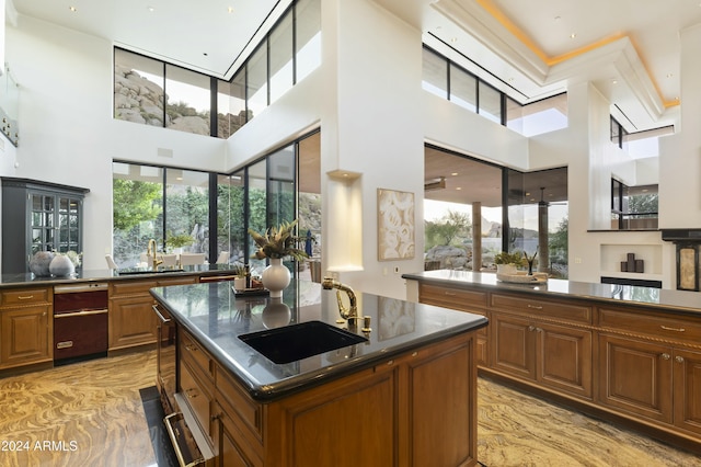 kitchen with sink, a towering ceiling, dark stone countertops, and an island with sink