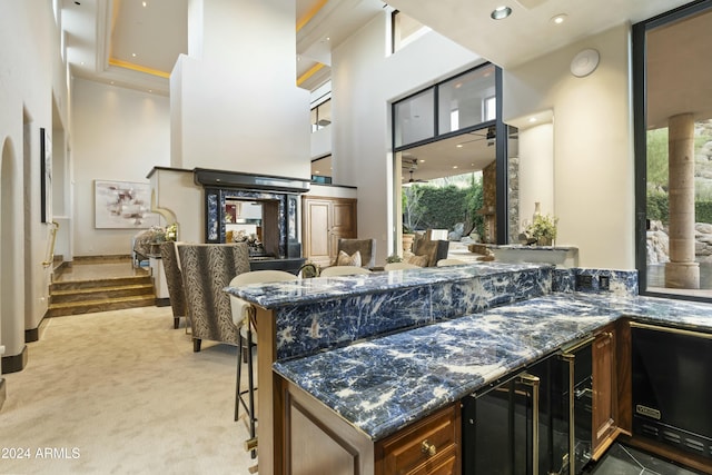 kitchen with light carpet, a kitchen breakfast bar, dark stone counters, a tray ceiling, and wine cooler