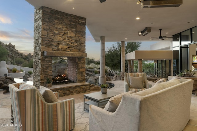 patio terrace at dusk with an outdoor stone fireplace and ceiling fan