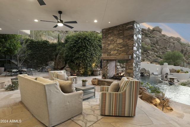 patio terrace at dusk with an outdoor stone fireplace and ceiling fan