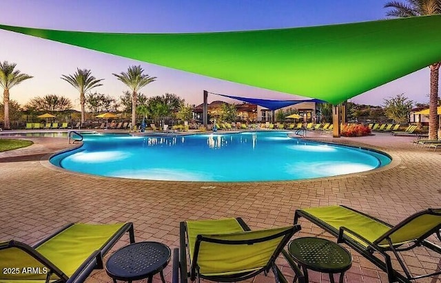 pool at dusk featuring a community pool and a patio