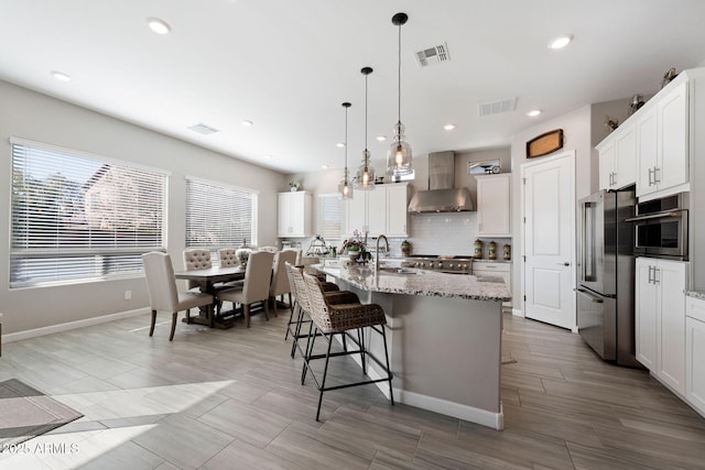 kitchen with premium appliances, visible vents, hanging light fixtures, an island with sink, and wall chimney exhaust hood