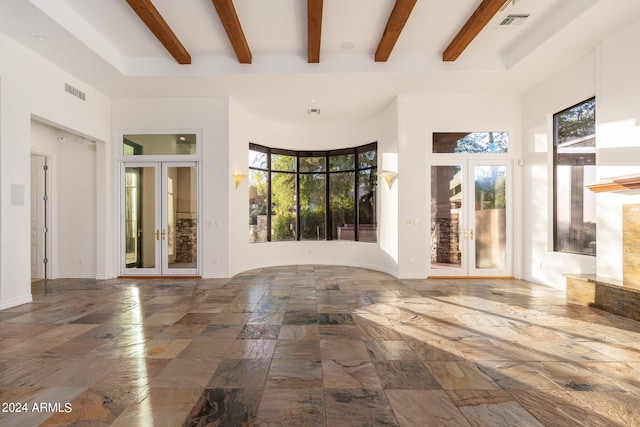 unfurnished living room featuring a high ceiling, beamed ceiling, and french doors