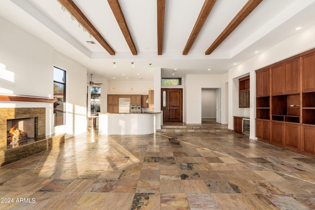 unfurnished living room featuring ceiling fan, beamed ceiling, a fireplace, and a towering ceiling