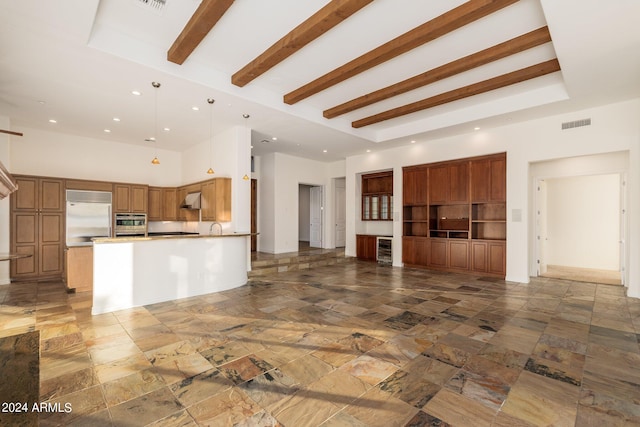 unfurnished living room with beam ceiling, a towering ceiling, and sink