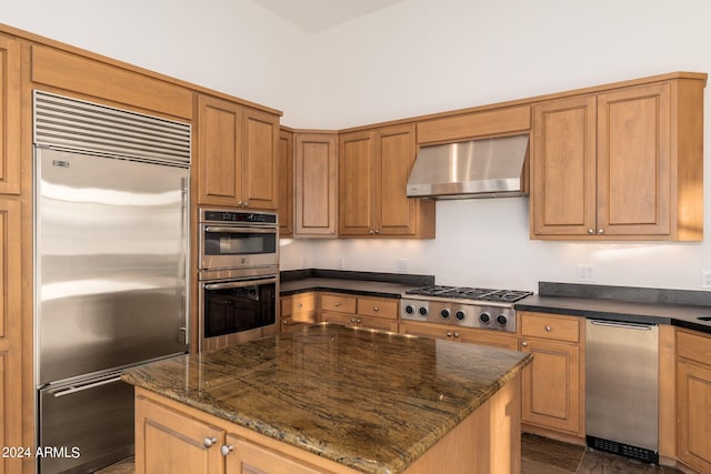 kitchen with appliances with stainless steel finishes, wall chimney exhaust hood, a kitchen island, and dark stone countertops