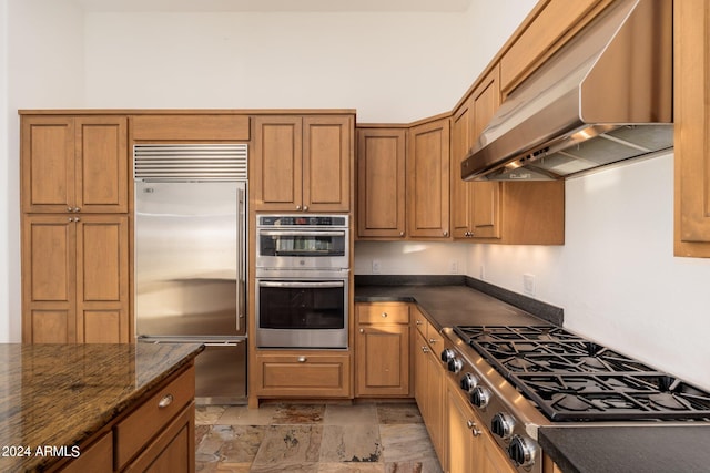 kitchen with dark stone countertops, appliances with stainless steel finishes, and wall chimney range hood