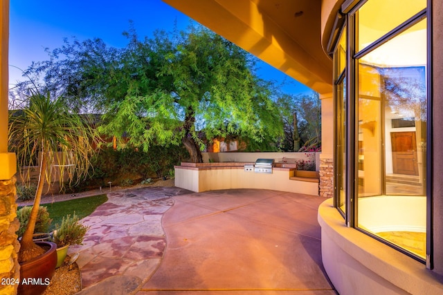 patio terrace at dusk featuring exterior kitchen and a grill