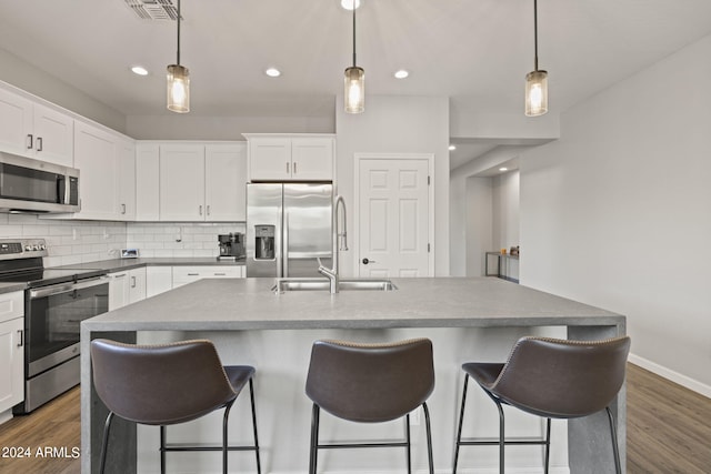 kitchen with an island with sink, stainless steel appliances, hanging light fixtures, and white cabinetry