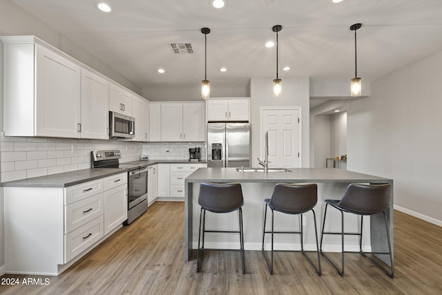 kitchen featuring light wood-type flooring, hanging light fixtures, white cabinetry, and stainless steel appliances