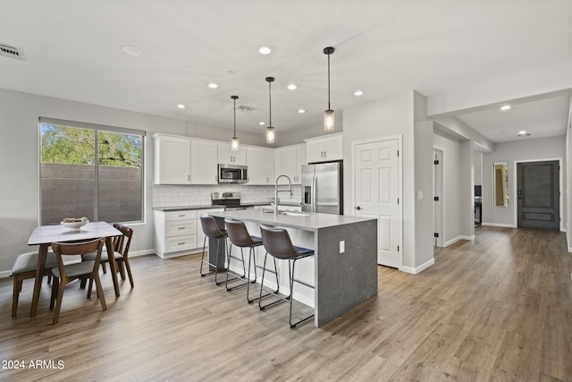 kitchen featuring hanging light fixtures, light hardwood / wood-style flooring, a kitchen island with sink, white cabinetry, and stainless steel appliances