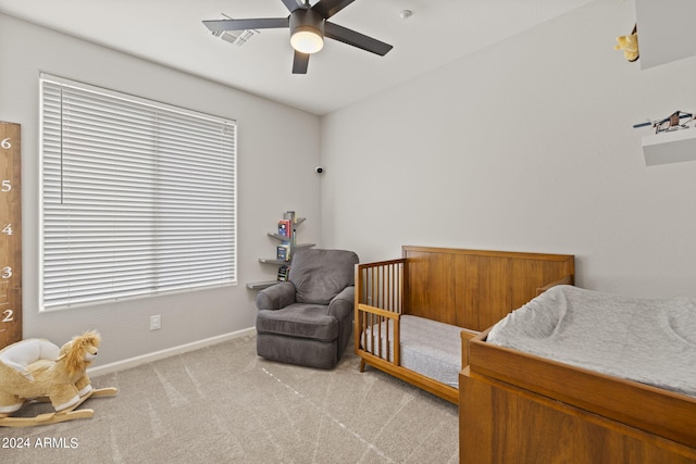 bedroom featuring ceiling fan, a crib, and light colored carpet