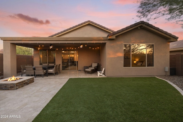 back house at dusk with ceiling fan, a yard, a patio area, and an outdoor fire pit