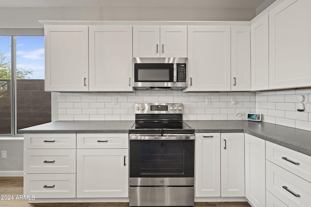 kitchen featuring decorative backsplash, white cabinets, appliances with stainless steel finishes, and hardwood / wood-style floors