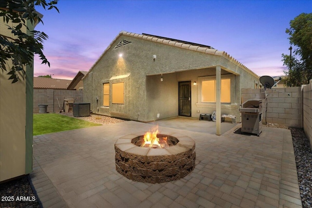 5026 S 235th Dr, Buckeye, AZ 85326 - back of house at dusk with stucco siding, an outdoor fire pit, a patio area, and a fenced backyard