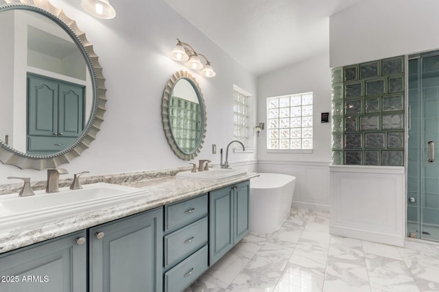 full bath featuring marble finish floor, a wainscoted wall, a soaking tub, vaulted ceiling, and a sink