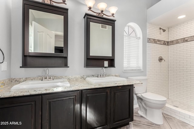 full bath with double vanity, tiled shower, a sink, and toilet