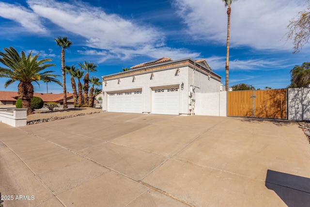 view of side of home with driveway, an attached garage, a gate, and stucco siding