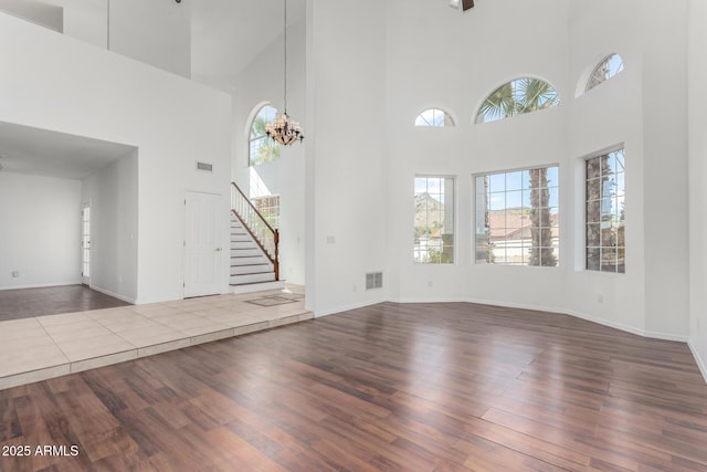 unfurnished living room with stairs, visible vents, an inviting chandelier, and wood finished floors