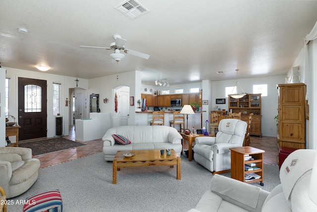 tiled living area with arched walkways, a textured ceiling, visible vents, and a ceiling fan