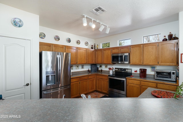 kitchen featuring a toaster, visible vents, brown cabinets, stainless steel appliances, and a textured ceiling