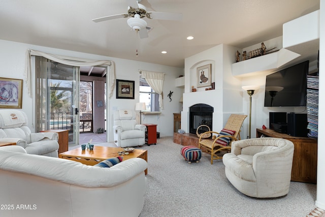 carpeted living room with a fireplace with raised hearth, a ceiling fan, and recessed lighting