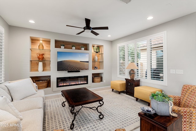 living area featuring a glass covered fireplace, built in shelves, recessed lighting, and ceiling fan