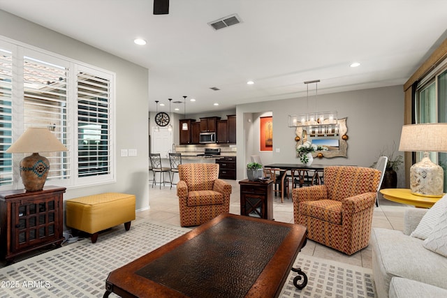 living room featuring light tile patterned floors, visible vents, recessed lighting, and ceiling fan with notable chandelier