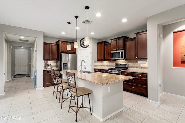 kitchen featuring a breakfast bar, a kitchen island with sink, a sink, stainless steel appliances, and dark brown cabinetry