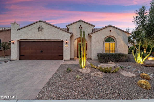 mediterranean / spanish home featuring a tile roof, an attached garage, driveway, and stucco siding