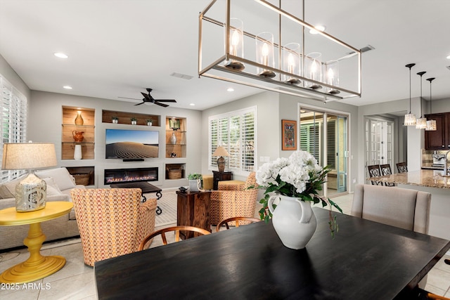 dining room with built in shelves, visible vents, recessed lighting, a glass covered fireplace, and ceiling fan with notable chandelier