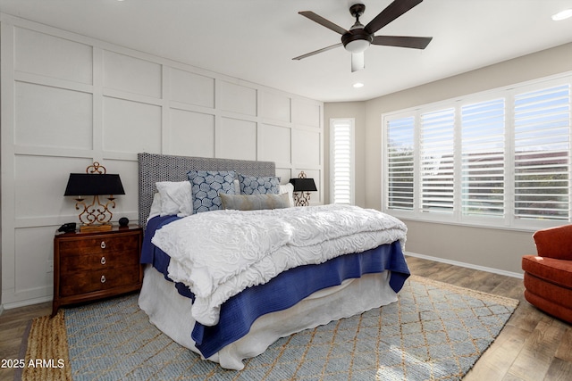 bedroom featuring baseboards, wood finished floors, a ceiling fan, and a decorative wall