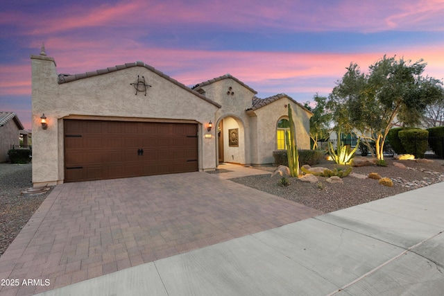 mediterranean / spanish-style house with decorative driveway, a garage, stucco siding, and a tile roof