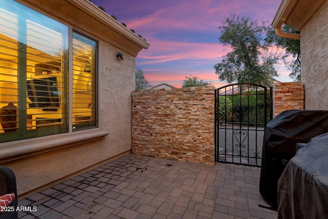 patio terrace at dusk featuring area for grilling and a gate