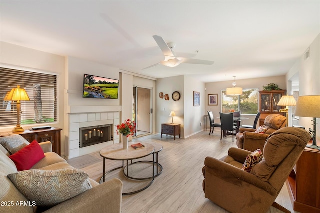 living room with baseboards, visible vents, a fireplace, ceiling fan, and light wood-type flooring