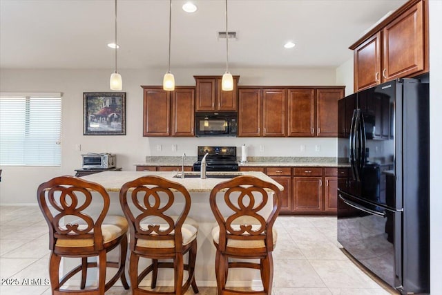 kitchen featuring decorative light fixtures, a kitchen island with sink, light tile patterned floors, black appliances, and light stone countertops