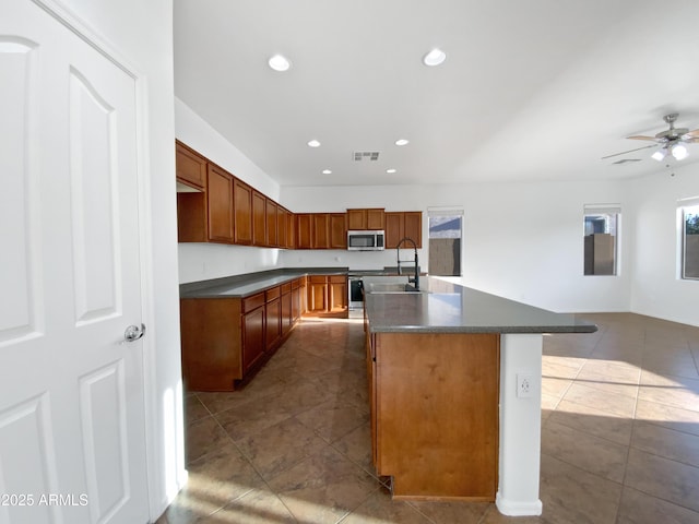 kitchen featuring tile patterned flooring, ceiling fan, appliances with stainless steel finishes, sink, and an island with sink