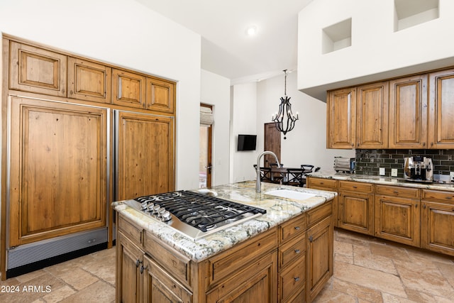 kitchen with light tile floors, stainless steel gas stovetop, tasteful backsplash, hanging light fixtures, and light stone counters