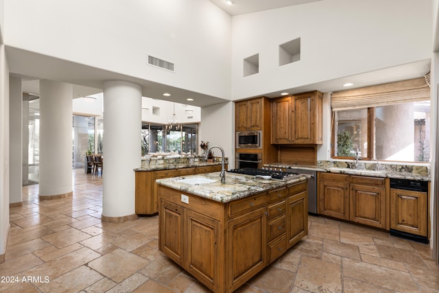 kitchen featuring light stone counters, stainless steel appliances, a kitchen island with sink, and a wealth of natural light