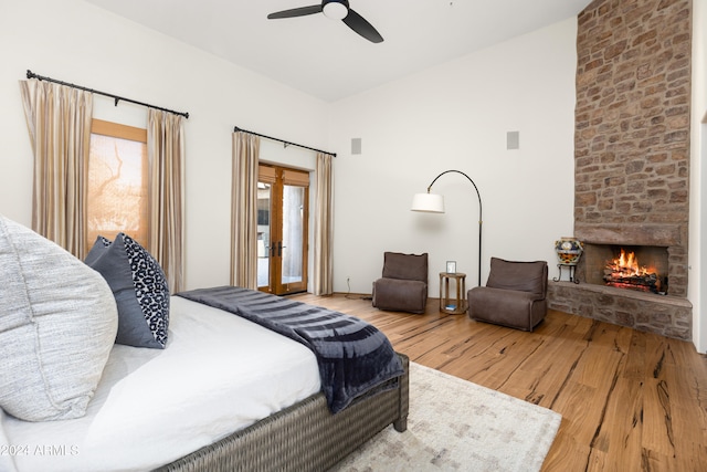 bedroom featuring french doors, light hardwood / wood-style floors, ceiling fan, and a stone fireplace