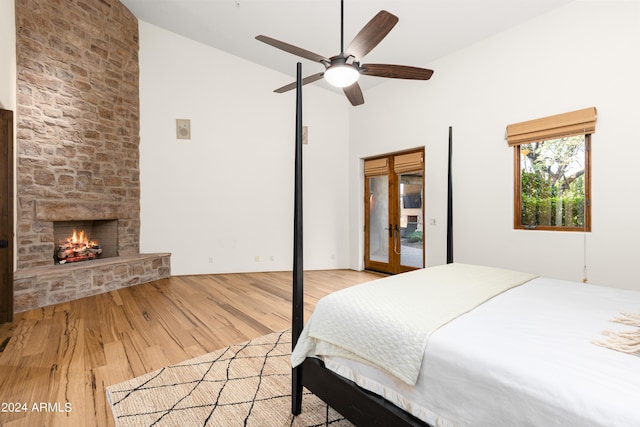 bedroom featuring high vaulted ceiling, light hardwood / wood-style floors, ceiling fan, and a stone fireplace