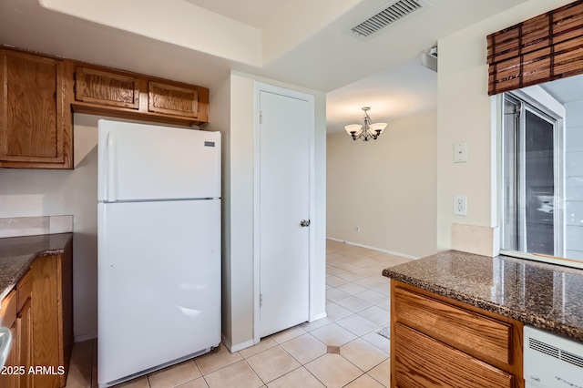 kitchen with pendant lighting, white refrigerator, dark stone countertops, a chandelier, and light tile patterned flooring