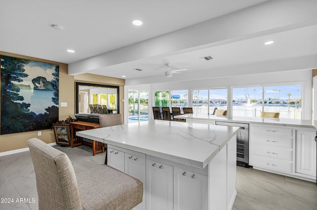 kitchen featuring light stone countertops, ceiling fan, beverage cooler, a kitchen island, and white cabinets