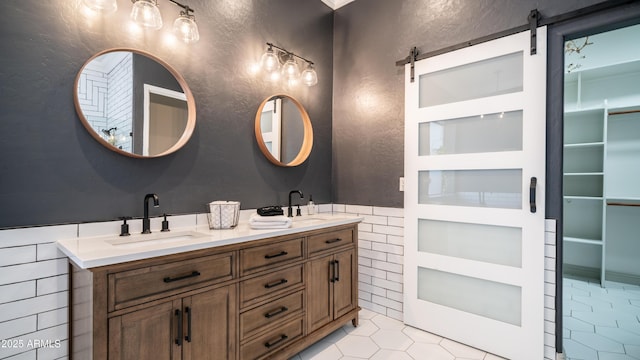 bathroom featuring tile patterned flooring, a sink, tile walls, wainscoting, and double vanity