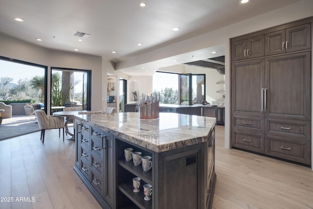 kitchen featuring a kitchen island, light stone countertops, light hardwood / wood-style floors, and dark brown cabinetry