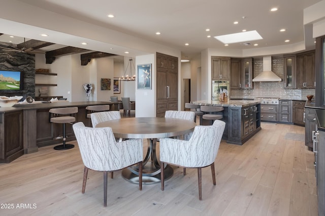 dining space featuring beam ceiling, light hardwood / wood-style flooring, a skylight, and a chandelier