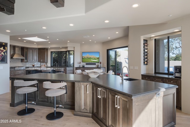 kitchen with a kitchen bar, plenty of natural light, wall chimney exhaust hood, and a spacious island