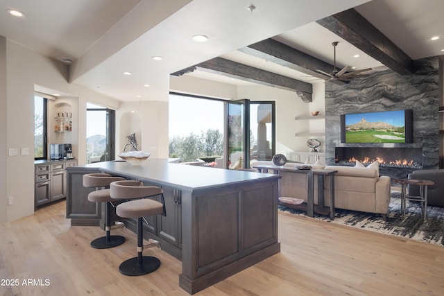 kitchen featuring a stone fireplace, light wood-type flooring, a center island, beamed ceiling, and plenty of natural light