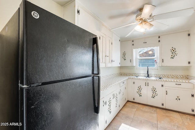 kitchen featuring black refrigerator, ceiling fan, sink, white cabinets, and light tile patterned floors